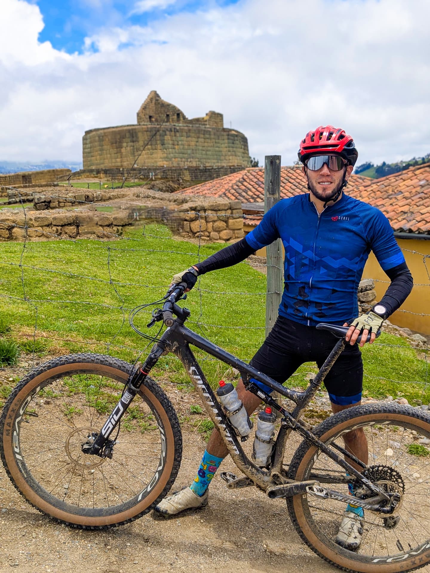 Ciclista con su bicicleta frente a las ruinas de Ingapirca